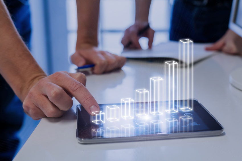 A team of business people analyzing a 3D augmented reality chart above a digital tablet screen illustrates Shift4 Payments' growing results and investment success.